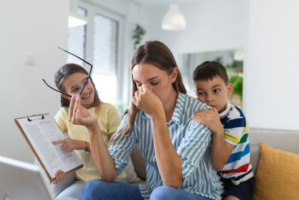 Frustrated mother working from home struggles with noisy, hyperactive children jumping on the couch — a relatable scene highlighting the need for Online ADHD Assessment and Treatment